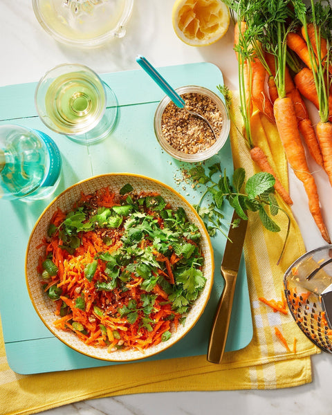 Grated Carrot Salad with Dukkah and herbs on a blue cutting board. 