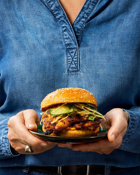Hands holding a plate with Korean BBQ Chicken Sandwich with Sesame slaw on a brioche bun