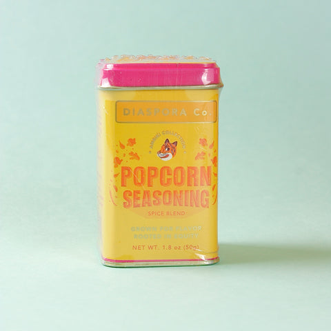 Yellow tin of Diaspora Co. popcorn seasoning on a light blue background