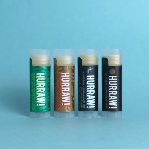 Four Hurraw! Lip Balm sticks displayed in a row with visible colors and textures corresponding to each flavor.