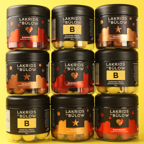 Multiple jars of Lakrids by Bulow chocolate coated licorice on a yellow background